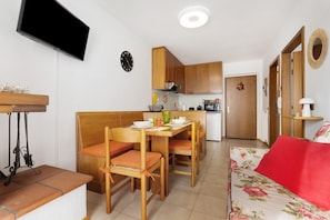 A compact living space with a dining area, kitchenette, and a sofa with a red cushion. - La Finestra sui Monti – Apartment with Terrace and Dolomiti di Brenta View (Breguzzo)