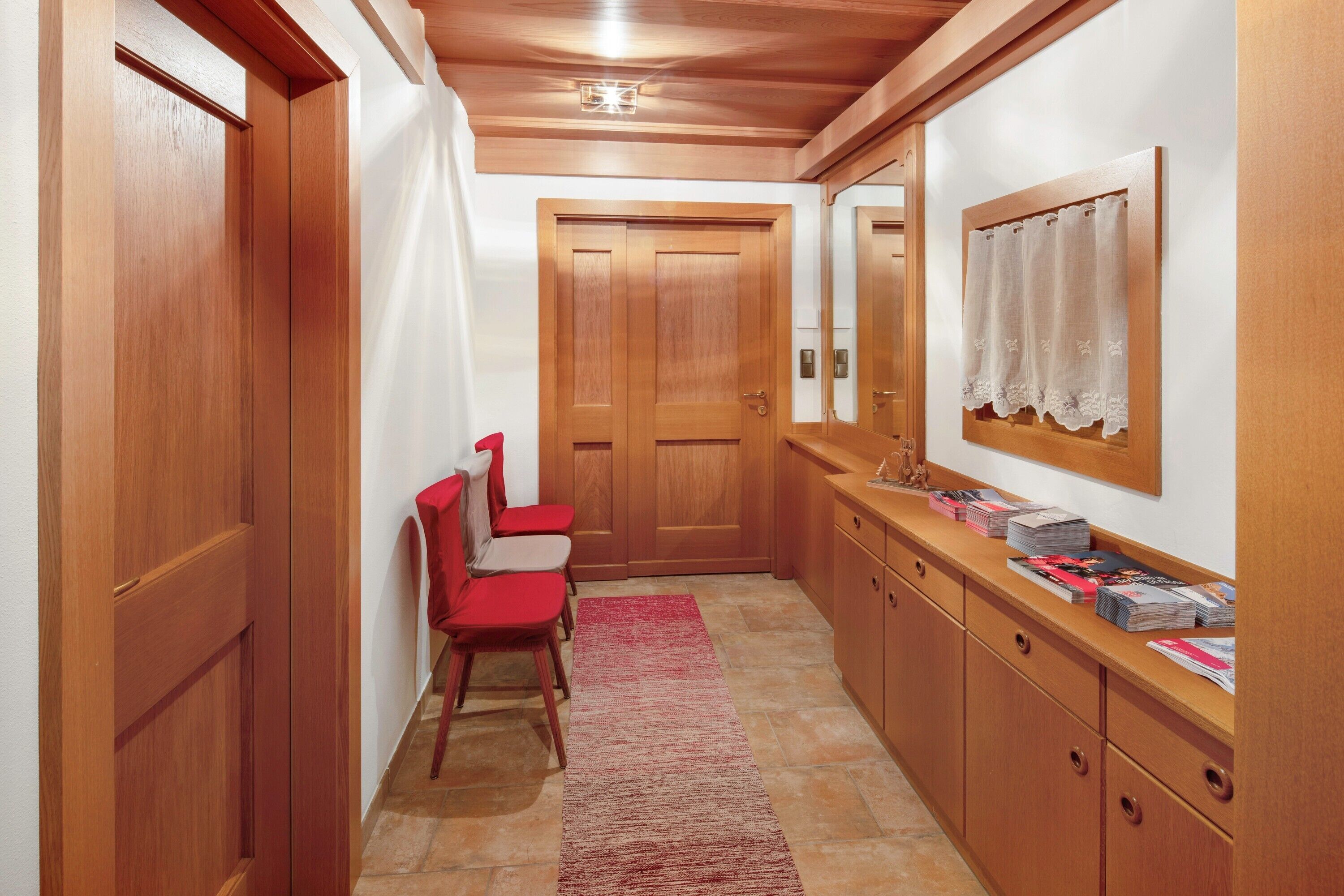 A hallway with wooden doors, a red chair, a rug, and a counter with magazines.