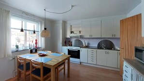 A compact kitchen with white cabinets, a dining table with chairs, and a large window with curtains. - 2 bedroom nice apartment in Hyltebruk (Hyltebruk)