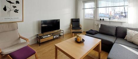 A modern living room with a flat-screen TV, a wooden coffee table, a grey sofa, and a purple cushioned chair.