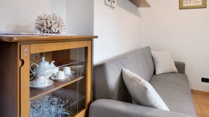 Ett vardagsrum med en grå soffa, ett träskåp med glasdörrar och en liten hylla med dekorativa föremål.