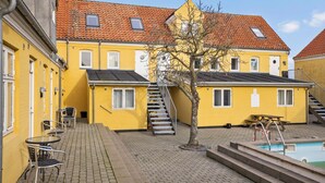 A yellow building with a tiled roof, a staircase, a tree, and a pool area. - Amazing apartment in Gudhjem with WiFi (Gudhjem)