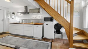 A compact kitchen with white cabinets, a microwave, a stove, and a sink. There's a wooden staircase leading to an upper level. - Amazing apartment in Gudhjem with WiFi (Gudhjem)