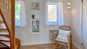 A room with a wooden staircase, a wicker chair, a cabinet with glass doors, and a window with white curtains. - Amazing apartment in Gudhjem with WiFi (Gudhjem)