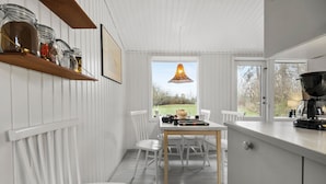 Ett kök med vita skåp, ett träbord och en hängande lampa.