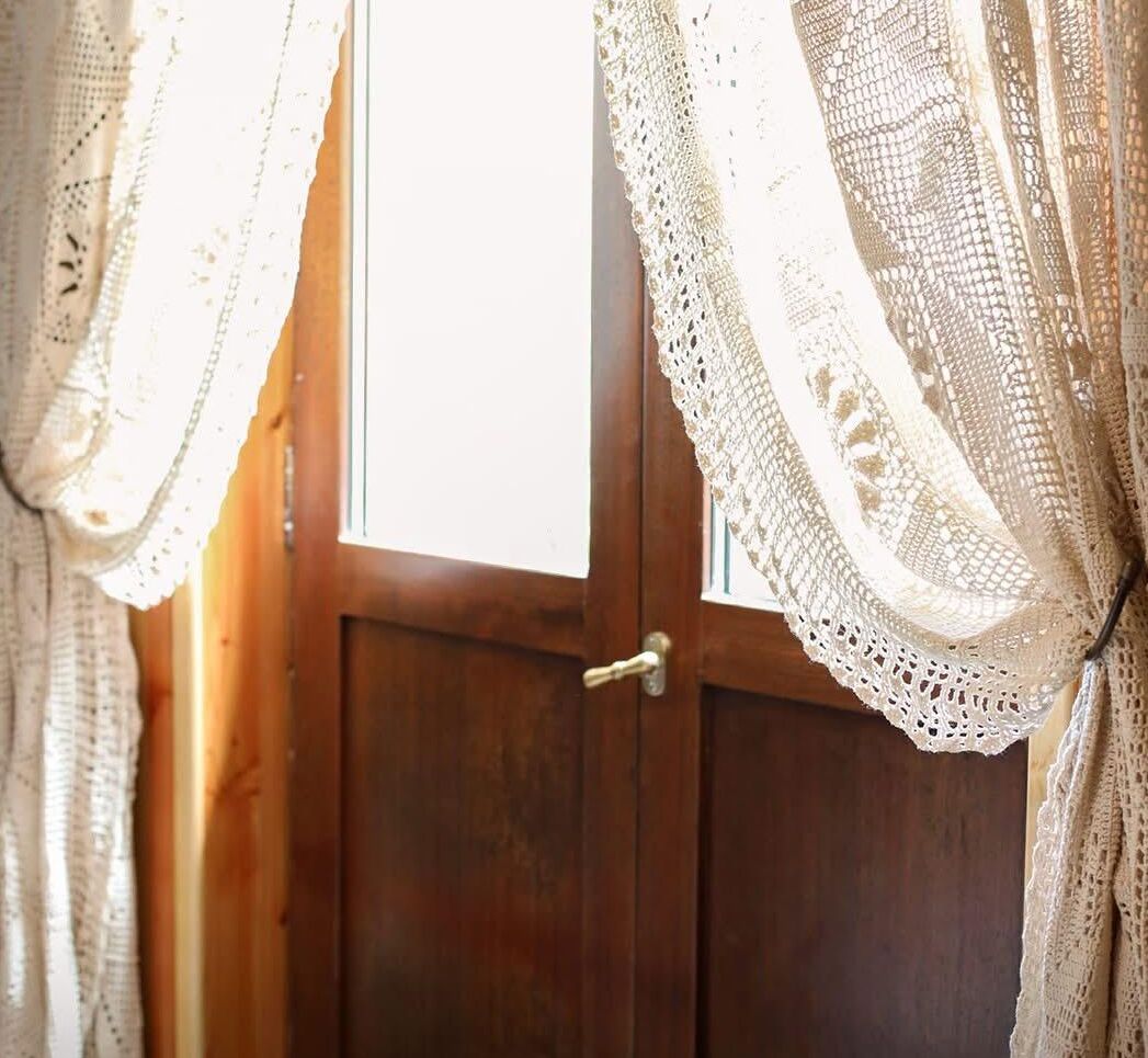 A wooden door with a brass handle, flanked by white lace curtains.