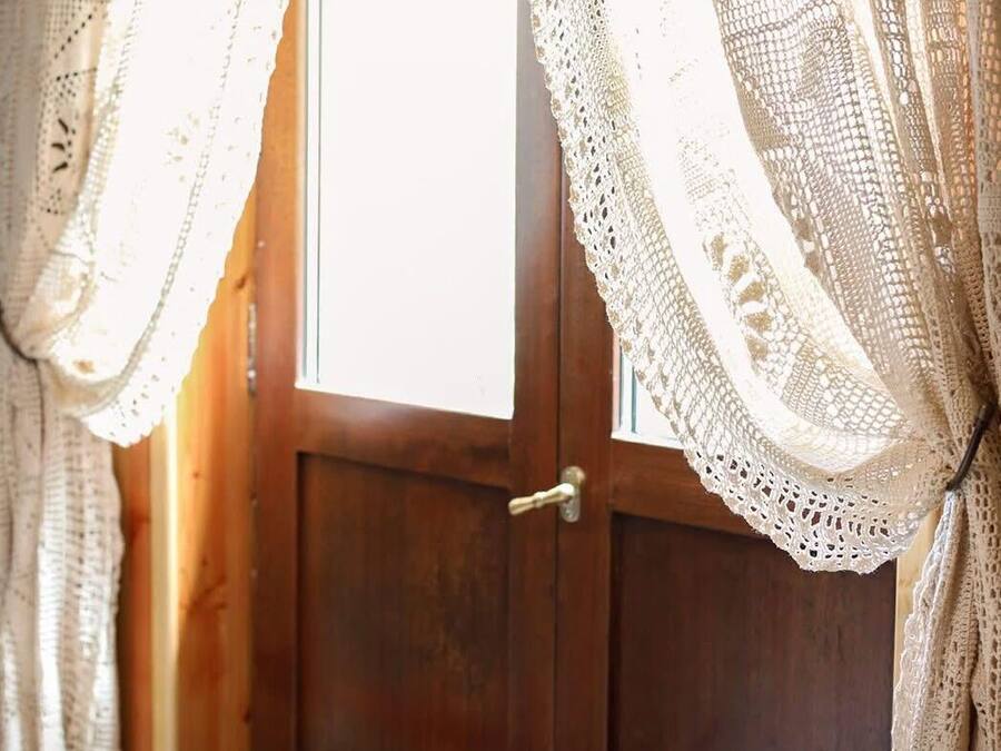 A wooden door with a brass handle, flanked by white lace curtains.