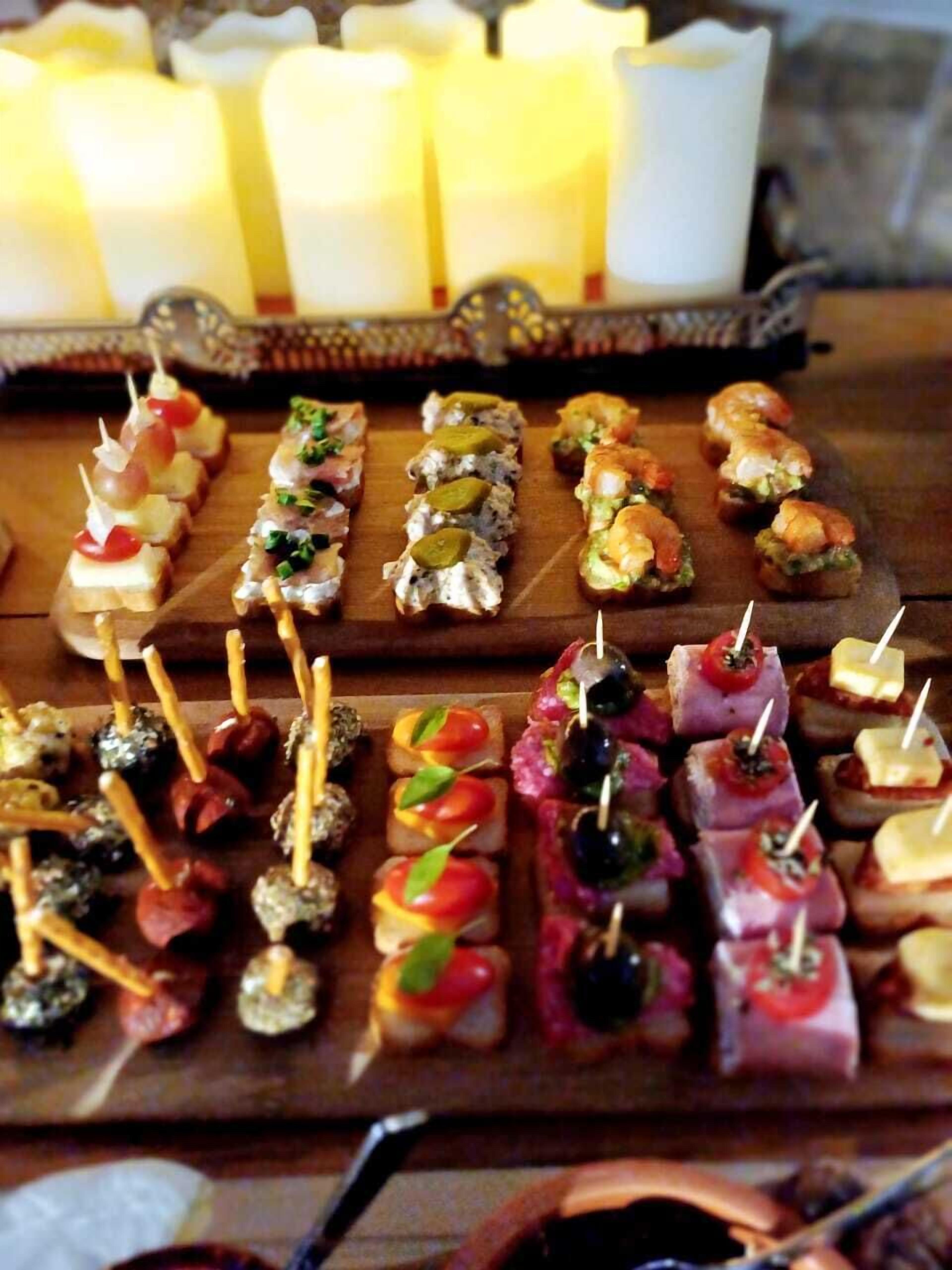 Diversos aperitivos dispuestos en una tabla de madera, con velas al fondo.