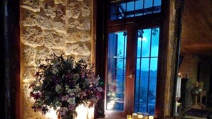 A cozy room with a stone wall, a wooden door, a table with a floral arrangement, and a couch with patterned cushions. - Laklouk 1808 lodge by Hansa (Laklouk)