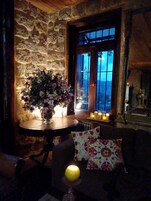 Una habitación acogedora con pared de piedra, puerta de madera, una mesa con un arreglo floral y un sofá con cojines estampados.