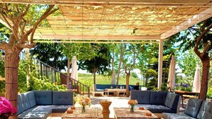 An outdoor patio with a covered seating area, wooden tables, and a stone fountain. - Laklouk 1808 lodge by Hansa (Laklouk)