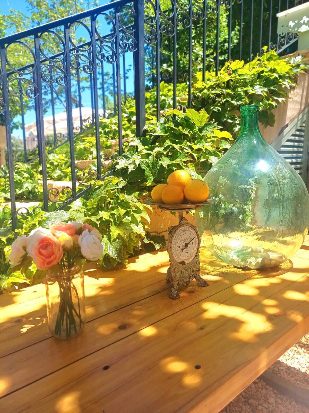 Una mesa de madera con un reloj, un jarrón de flores y una botella en un balcón.