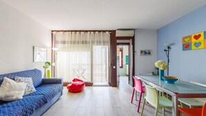 Un salon avec un canapé, une table à manger, des chaises colorées et une vue sur l’extérieur, visible à travers une porte.