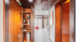 Un couloir avec des portes en bois, une étagère ornée d’objets décoratifs et un sac rouge posé sur le sol.
