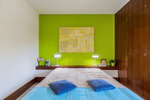Une chambre à coucher avec un lit, deux lampes de chevet, un mur vert et une armoire en bois.