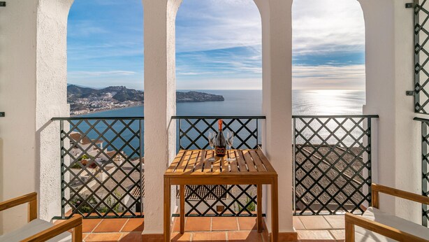 A balcony with a table and chairs, overlooking a coastal cityscape.