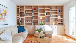 A living room with a sofa, two round tables, and a bookshelf filled with books and decorative items.