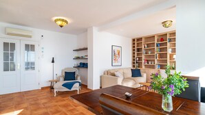 A living room with a wooden floor, a beige sofa, a coffee table, and a bookshelf filled with books and decorative items.
