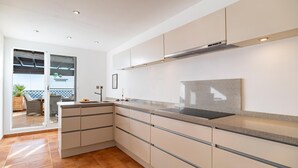 A modern kitchen with white cabinets, a stainless steel range hood, and a large window overlooking a balcony.