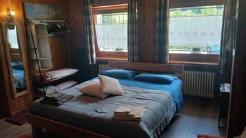 Una stanza in legno con un letto, una panca, un termosifone e una finestra con tende.