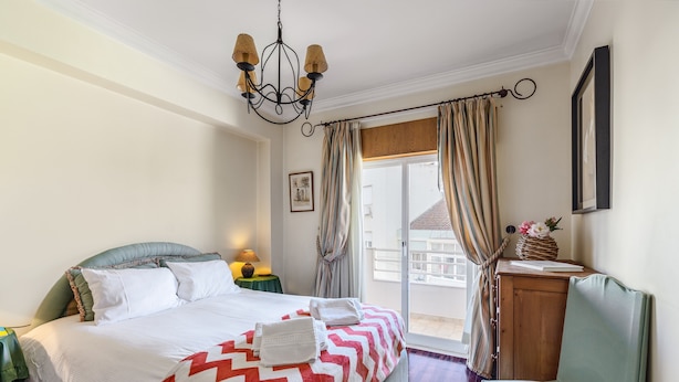 Habitación de hotel con cama, una silla, escritorio, candelabro, cortinas y vistas al balcón.