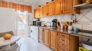 Una cocina con armarios de madera, una encimera, un lavabo, una lavadora y una zona de comedor con mesa y sillas.