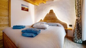Una cama con estructura de madera, cabecera blanca, toallas azules y una mesita de noche con lámpara.
