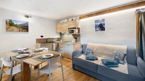 Un espacio habitable compacto con zona de comedor, kitchenette y sofá con mantas.