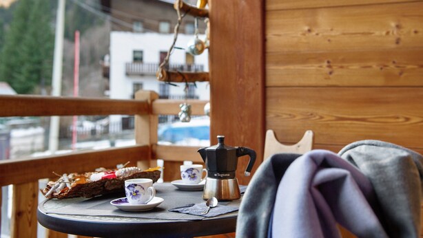 Una mesa de madera con una cafetera, tazas y un plato de comida en un balcón con vistas a la montaña.