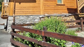 Una cabaña de madera con balcón, cimientos de piedra y un paisaje montañoso al fondo.