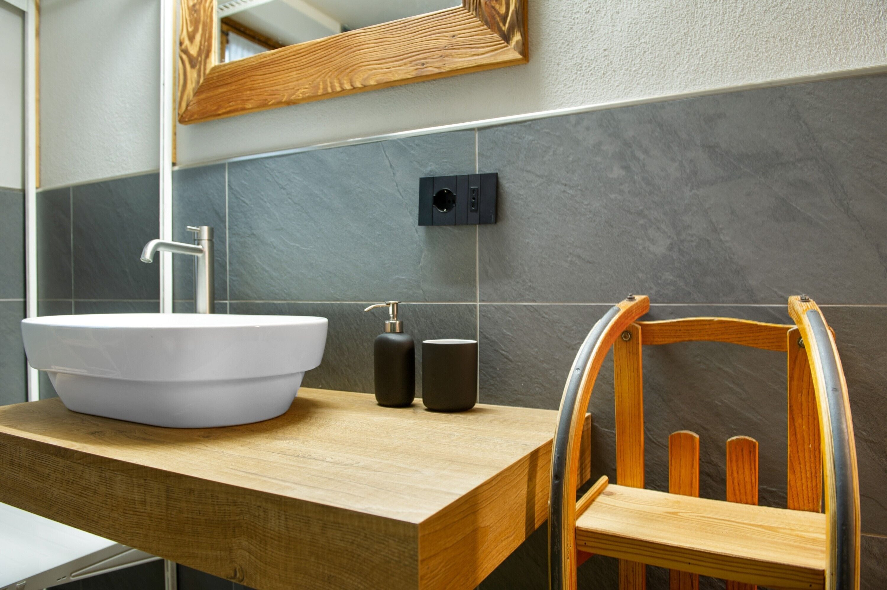 Une salle de bain moderne avec un grand lavabo blanc, une chaise en bois et un miroir avec un cadre en bois.