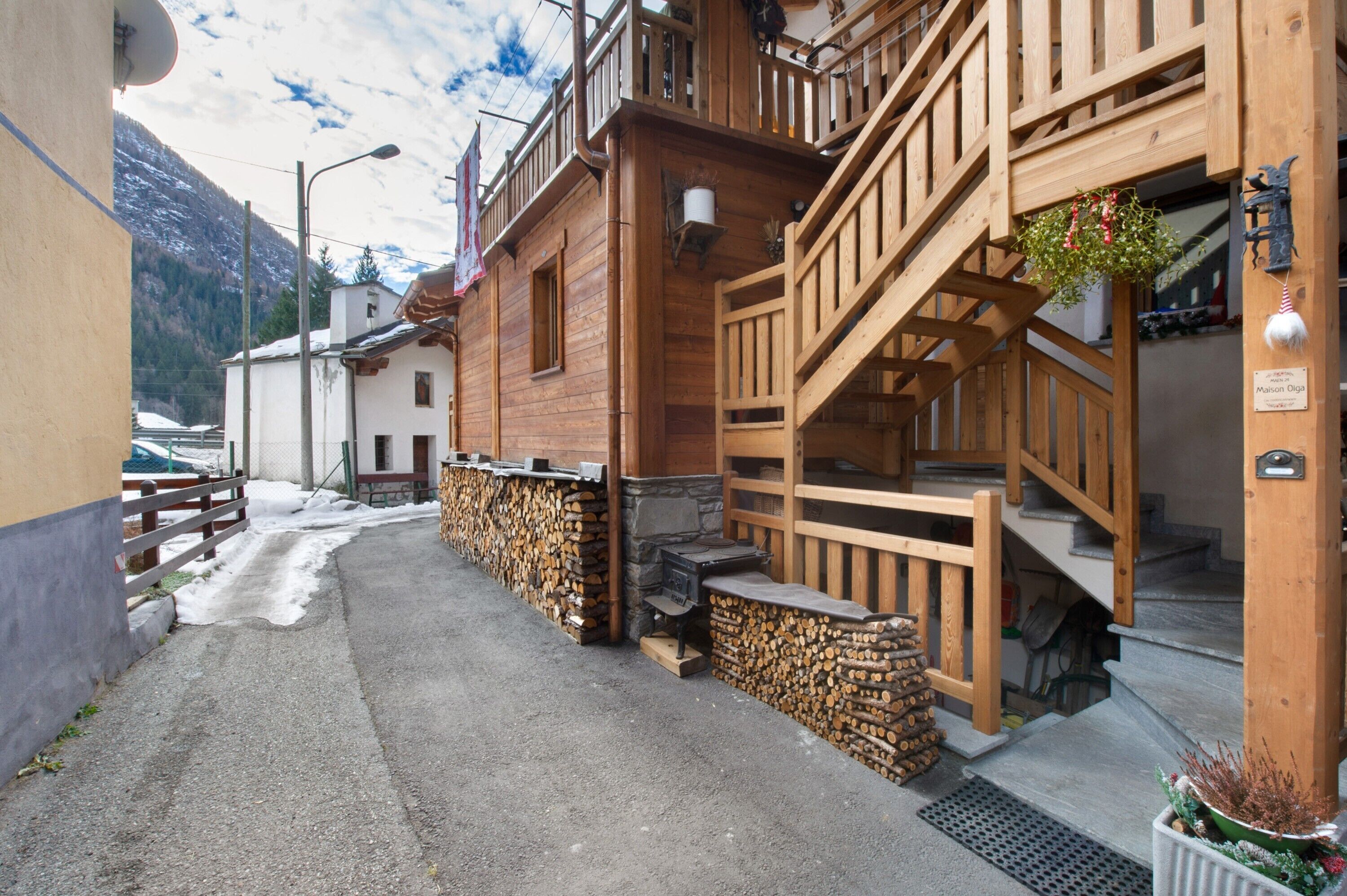 Un bâtiment en bois avec un escalier, une enseigne indiquant « Maison Digé », et une chaîne de montagnes en arrière-plan.