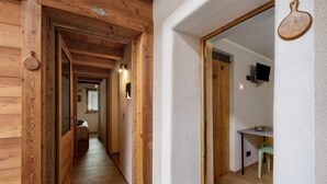 Een houten interieurhal met een deur naar een kamer, een klein tafeltje met een stoel, en een aan de muur bevestigde televisie.
