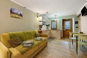 Un salon confortable avec un canapé, une table à manger et des chaises, un coin cuisine et un téléviseur fixé au mur.