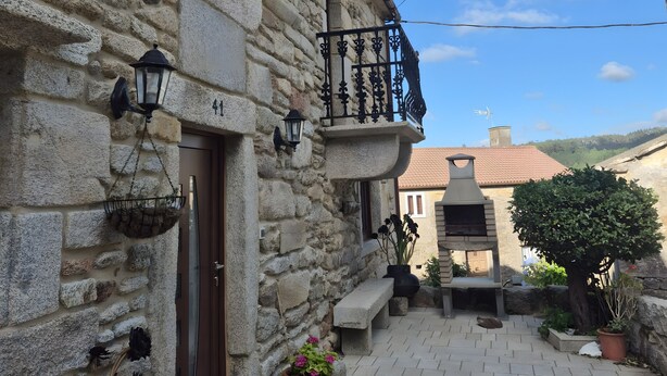 A stone building with a balcony, a door, and a small garden area with potted plants. - Country House 'Fidalgo' with Mountain View, Private Terrace and Wi-Fi (Vimianzo)