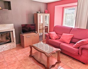 Ein Wohnzimmer mit Kamin, Fernseher, Holzschrank, rosa Sofa und einem kleinen Tisch.