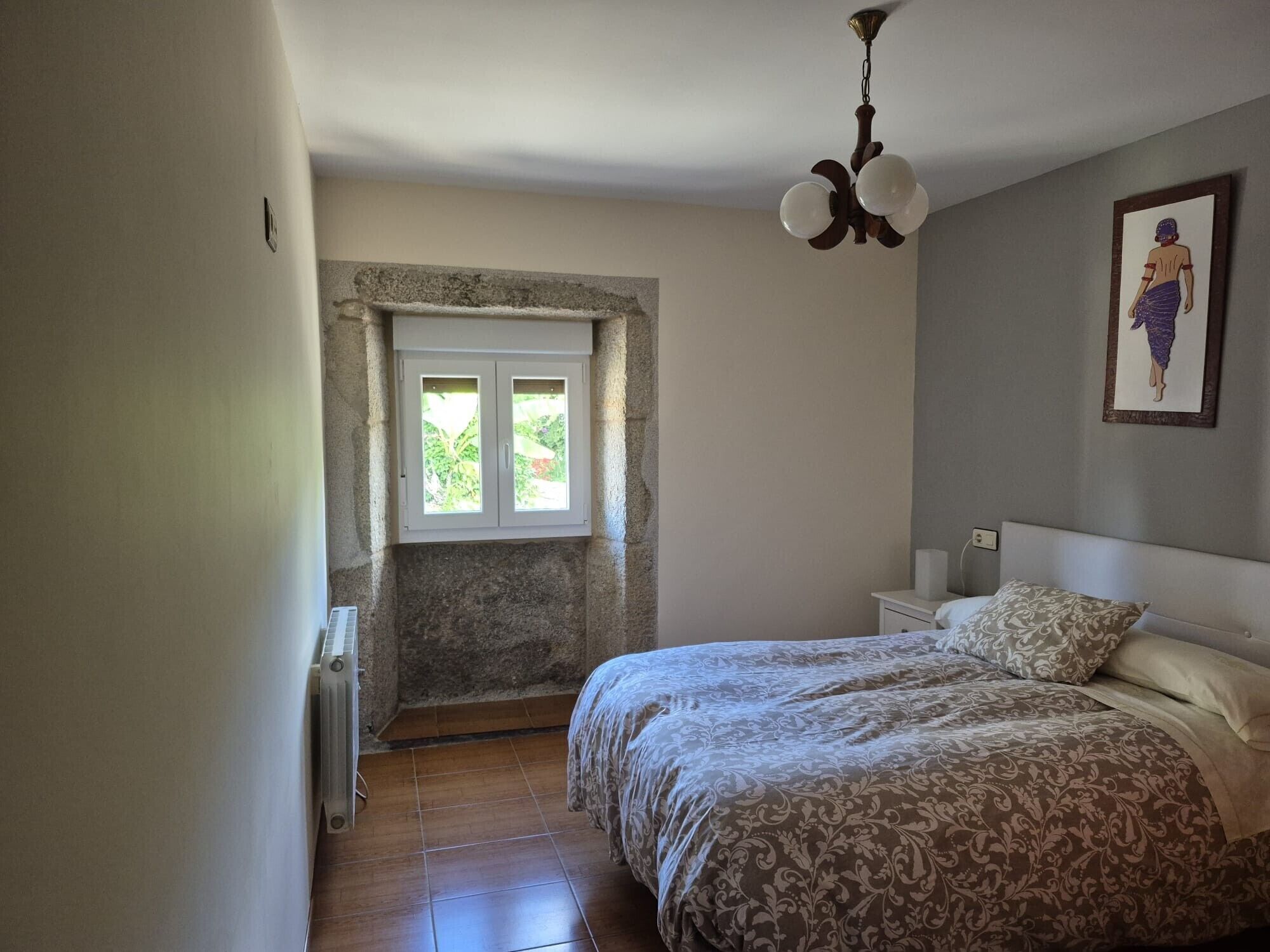 Une chambre à coucher comprenant un lit, une table de chevet, une lampe fixée au mur, un ventilateur de plafond et une fenêtre donnant sur un paysage agréable.