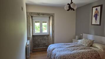Une chambre à coucher comprenant un lit, une table de chevet, une lampe fixée au mur, un ventilateur de plafond et une fenêtre donnant sur un paysage agréable.