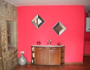 Une pièce avec un mur en pierre, un mur rouge, un meuble en bois doté de tiroirs, et deux miroirs en forme de losange accrochés au mur rouge.