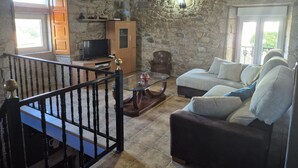A rustic living room with stone walls, a wooden ceiling, a TV, a sofa, and a staircase. - Country House 'Fidalgo' with Mountain View, Private Terrace and Wi-Fi (Vimianzo)