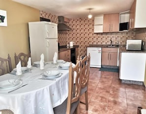 Un coin repas avec une table dressée pour quatre personnes, un réfrigérateur, un four à micro-ondes et un lave-vaisselle.