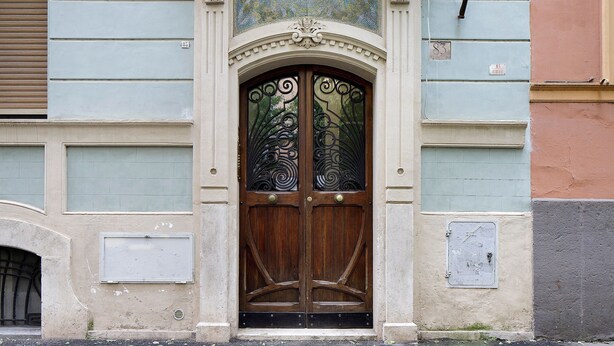 A building with a large wooden double door, a small window above the door, and a number '83' on the wall.