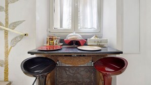A corner of a room with a window, a table with plates and a glass, and two chairs.