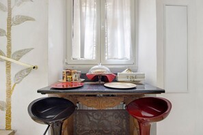 Un coin de pièce avec une fenêtre, une table avec des assiettes et un verre, et deux chaises.
