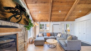 Una sala de estar moderna con chimenea de piedra, un sofá seccional gris, una mesa redonda para café y techo de madera.