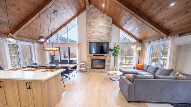 Un amplio salón con chimenea de piedra, techo de madera y ventanas grandes.