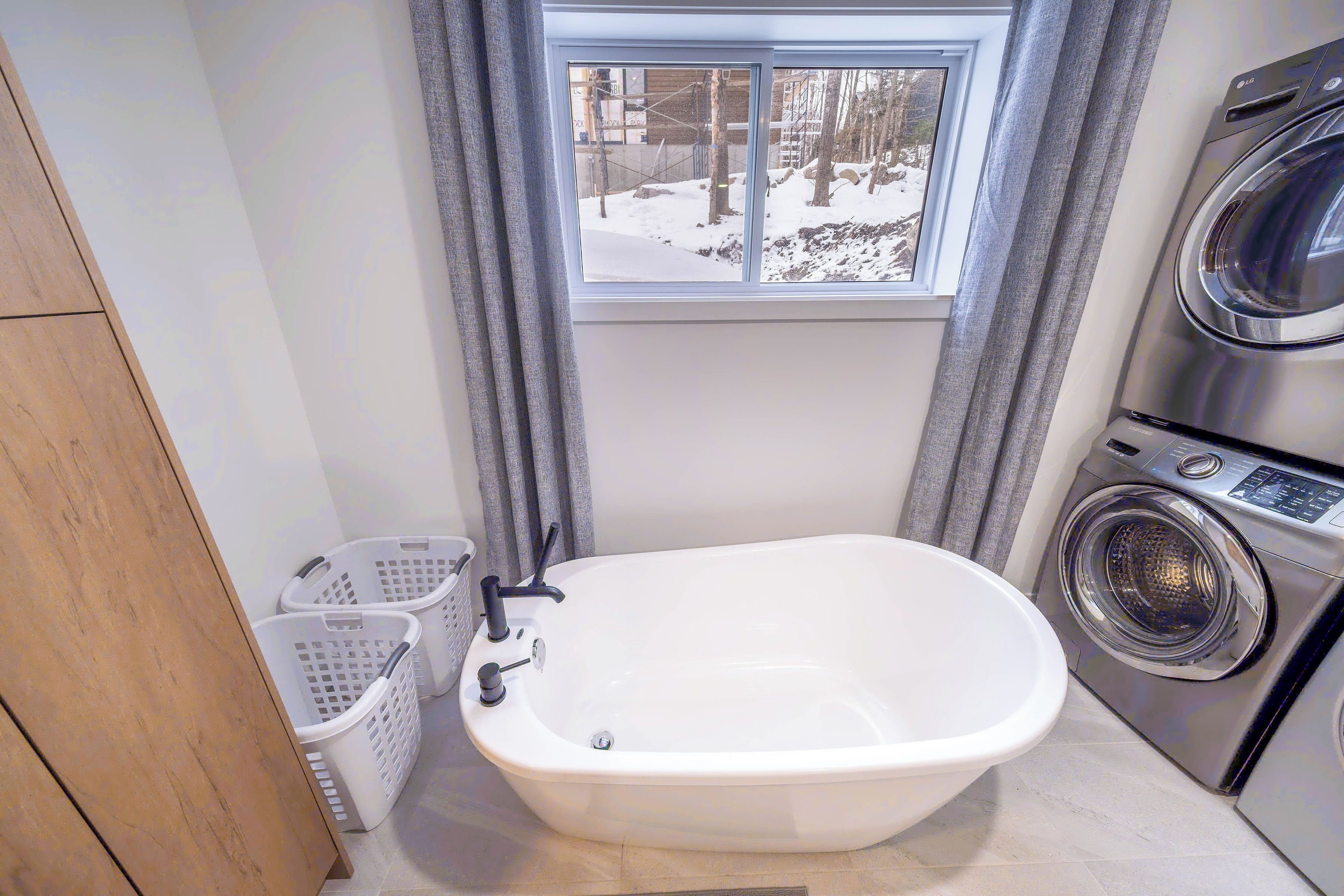 Ett badrum med ett fristående badkar, en tvättmaskin och ett fönster med utsikt över ett snötäckt landskap.