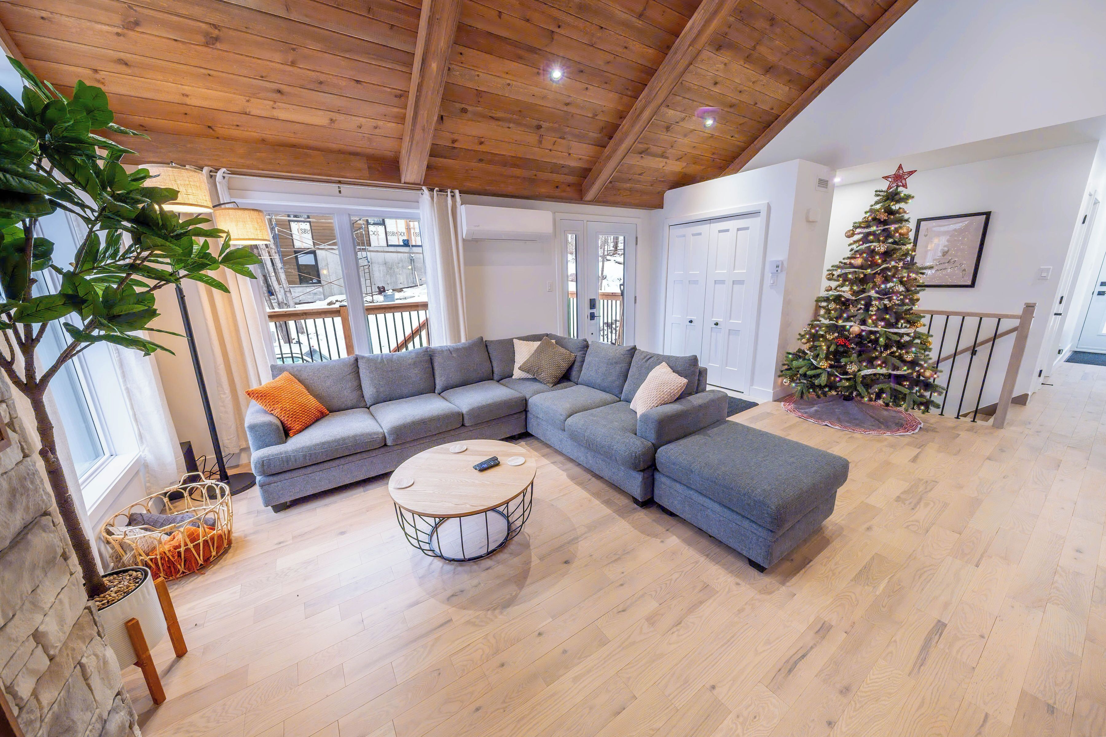 Un salon moderne avec un canapé d’angle, une table basse ronde et un plafond en bois.