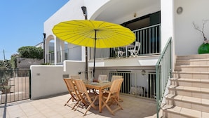 Eine Terrasse mit Tisch und Stühlen, einem gelben Sonnenschirm und einer Treppe.