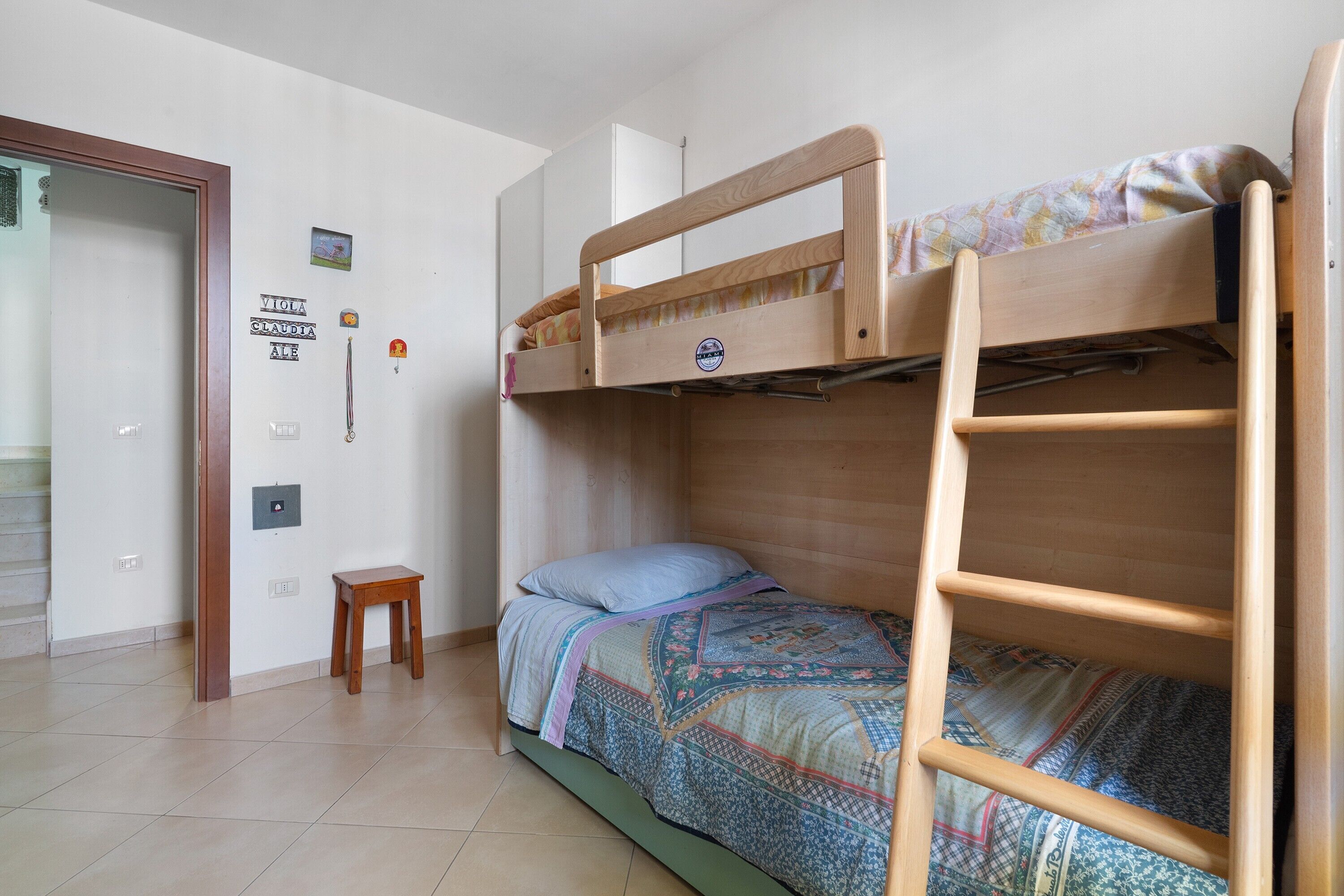A room with a bunk bed, a small wooden stool, and a wall-mounted light switch.